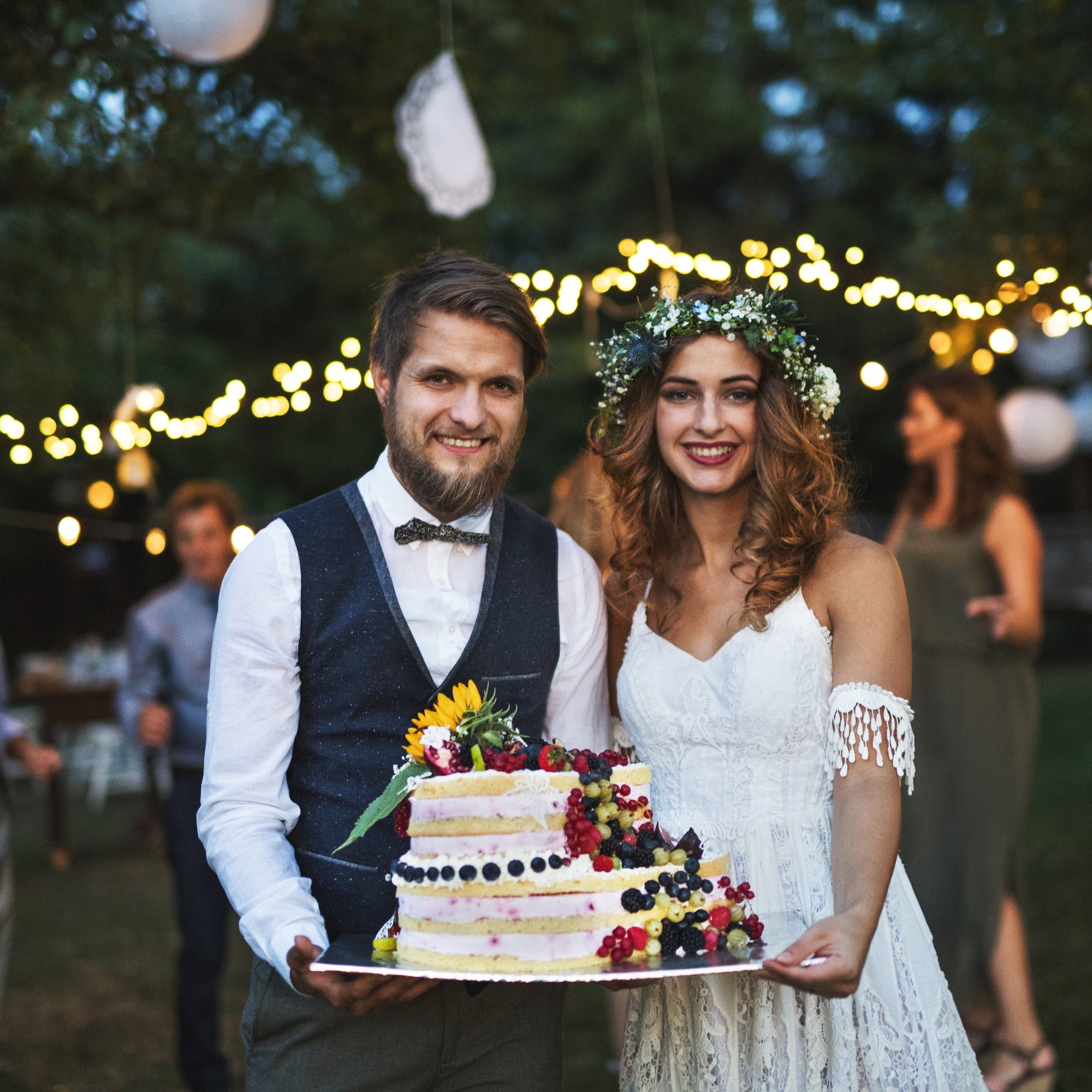 A couple holding a cake at an outdoor wedding reception