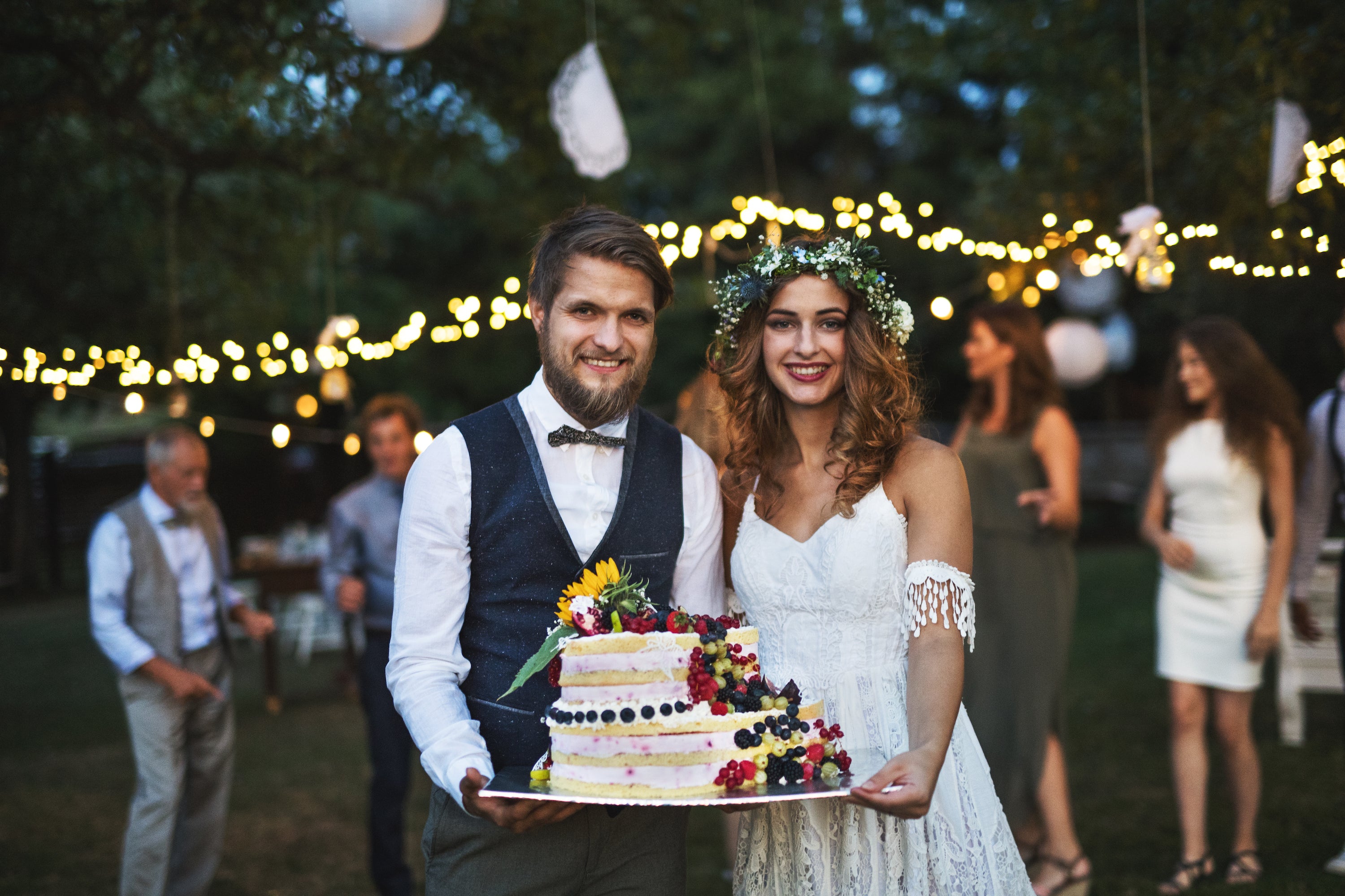 A couple holding a cake at an outdoor wedding reception